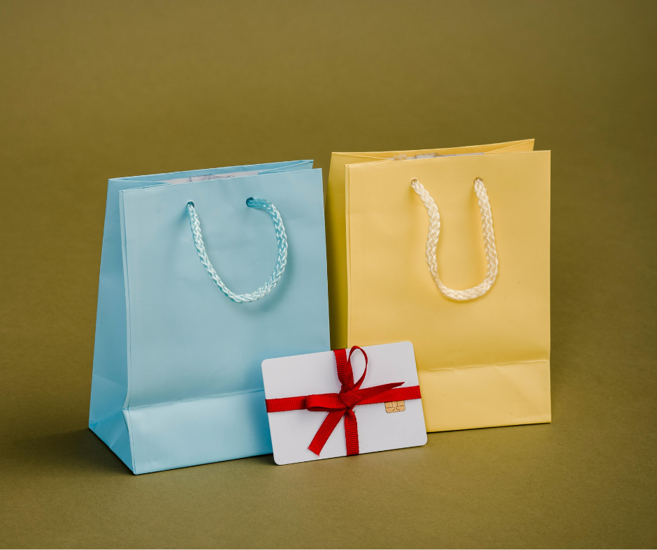 Blue and yellow gift bags with braided handles next to a white gift card tied with a red ribbon, vintage clothing theme.
