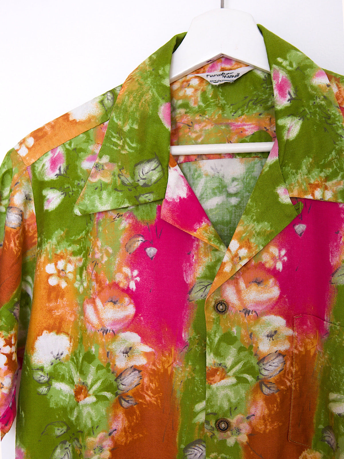 Green, orange, and pink cotton vintage Hawaiian shirt with bright floral print and short sleeves.